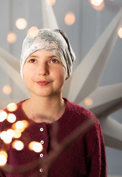 Emilka w jasnej chuście na głowie, portret w miękkim świetle, w tle rozmyte światełka.